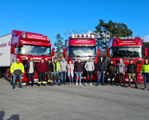 Gruppe kursdeltakere foran tre lastebiler hos Flekkefjord Opplæringssenter